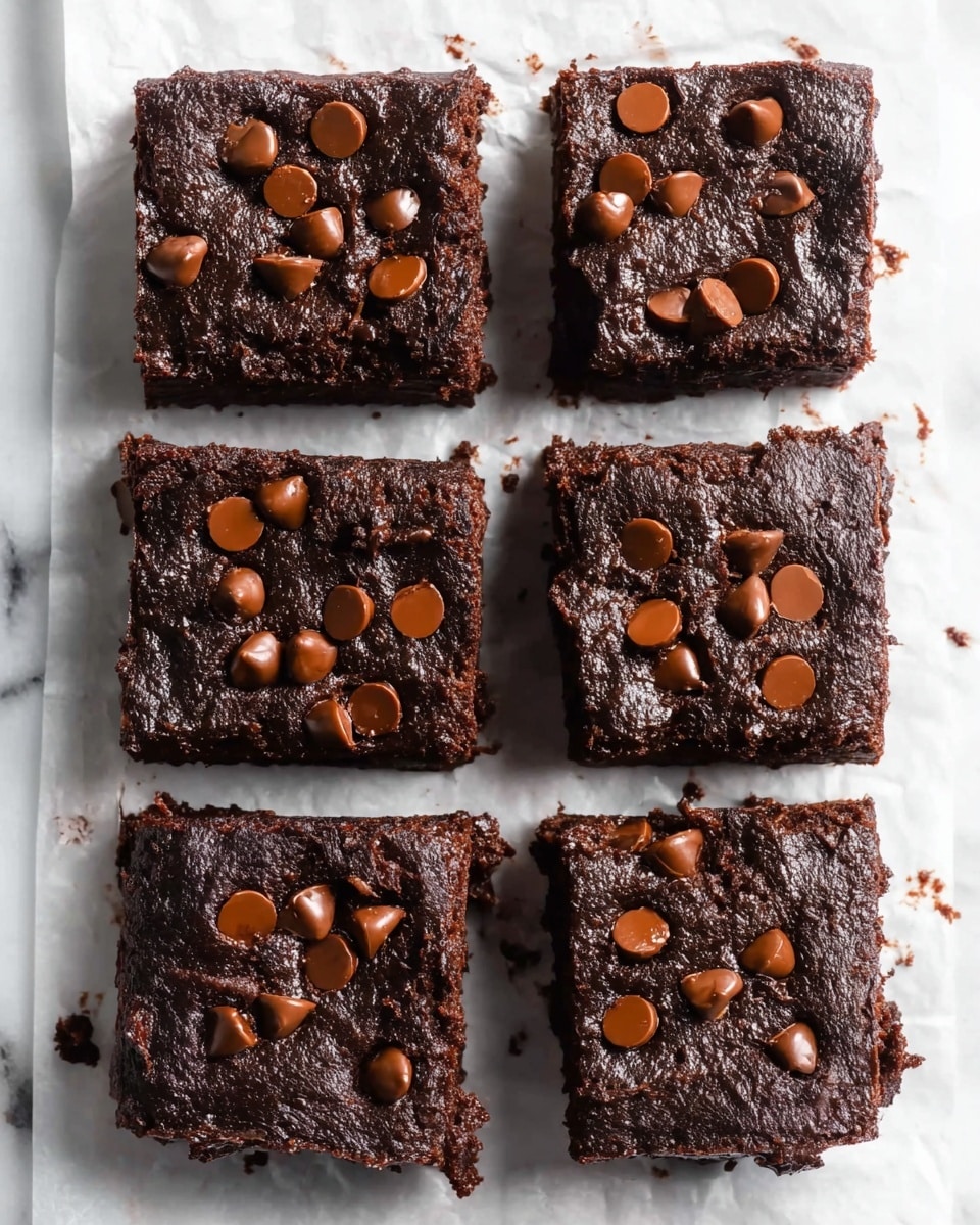 The image shows six thick square brownies arranged in two columns and three rows on white parchment paper over a white marbled surface. Each brownie is dark brown, rich, and fudgy with a slightly rough texture on the sides and smoother tops. Scattered across the top of each brownie are shiny milk chocolate chips that add small rounded shapes and a glossy contrast to the matte chocolate base. The brownies look moist and dense, with some chocolate chips slightly melted and others holding their form. The image is taken from above, showing all six brownies clearly with small gaps between them. photo taken with an iphone --ar 4:5 --v 7