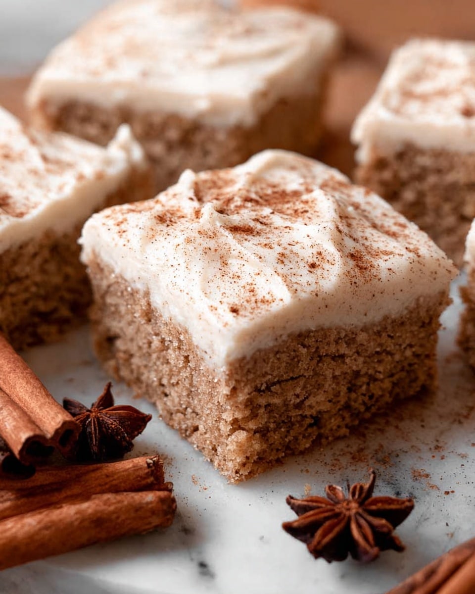 The image shows a close-up view of square pieces of spice cake with a thick, creamy layer of white frosting on top, lightly sprinkled with brown spice powder. The cake layer has a soft, crumbly texture with a light brown color, and the frosting looks smooth and fluffy. The pieces are arranged together on a white marbled surface, with some cinnamon sticks and star anise nearby, adding a warm, cozy feel. photo taken with an iphone --ar 4:5 --v 7