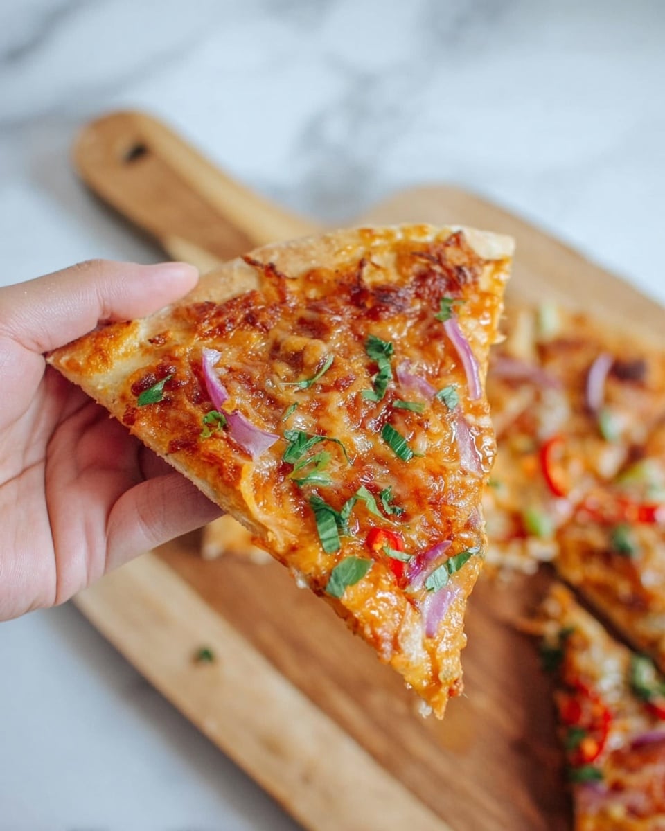 A close-up of a slice of pizza held by a woman's hand, showing a thin crust with a golden-brown edge. The pizza slice has a layer of melted light orange cheese with some melted spots on top. There are thin slices of red chili peppers, small pieces of chopped green herbs scattered over it, and a few thin red onion strips. The background shows a blurred pizza on a wooden cutting board, placed on a surface with a white marbled texture. Photo taken with an iphone --ar 4:5 --v 7