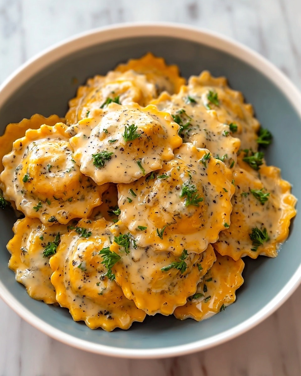 A white bowl filled with round ravioli pasta, each piece a golden orange color with crimped edges, coated in a creamy sauce speckled with green herbs and black pepper. The sauce covers all the ravioli, giving them a rich and smooth texture, while small bits of chopped fresh parsley are scattered on top for color contrast. The bowl sits on a white marbled surface, and the overall look is warm and inviting. photo taken with an iphone --ar 4:5 --v 7