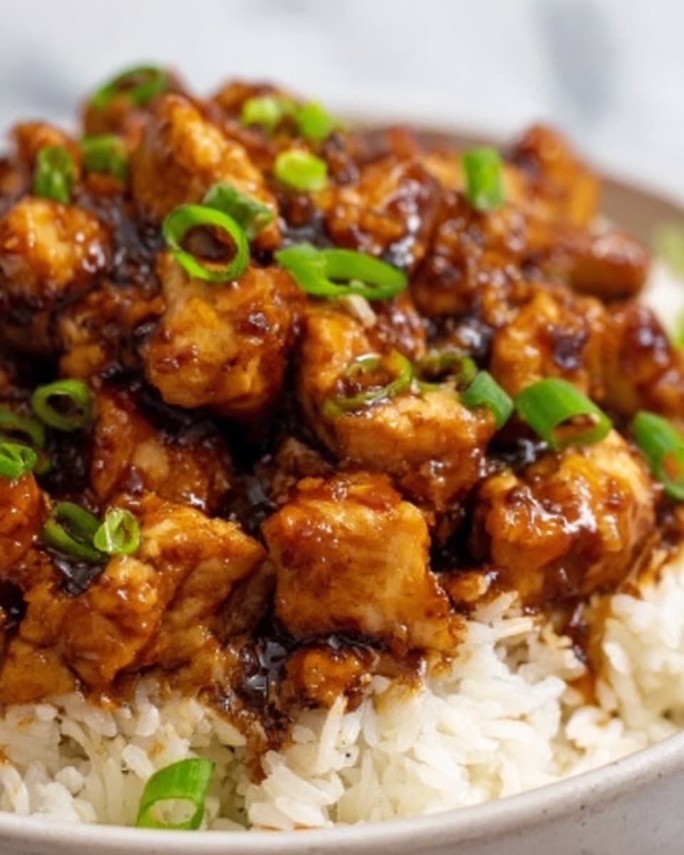 The image shows a close-up of a dish with three main layers. The bottom layer is white rice with a fluffy texture, spread evenly across the white plate. On top of the rice, there are chunks of grilled chicken that have a shiny, dark brown glaze with some slightly caramelized edges. Scattered on the chicken pieces are small, thin cuts of green onions, adding a fresh green color and a touch of texture. The background is a white marbled surface. Photo taken with an iphone --ar 4:5 --v 7
