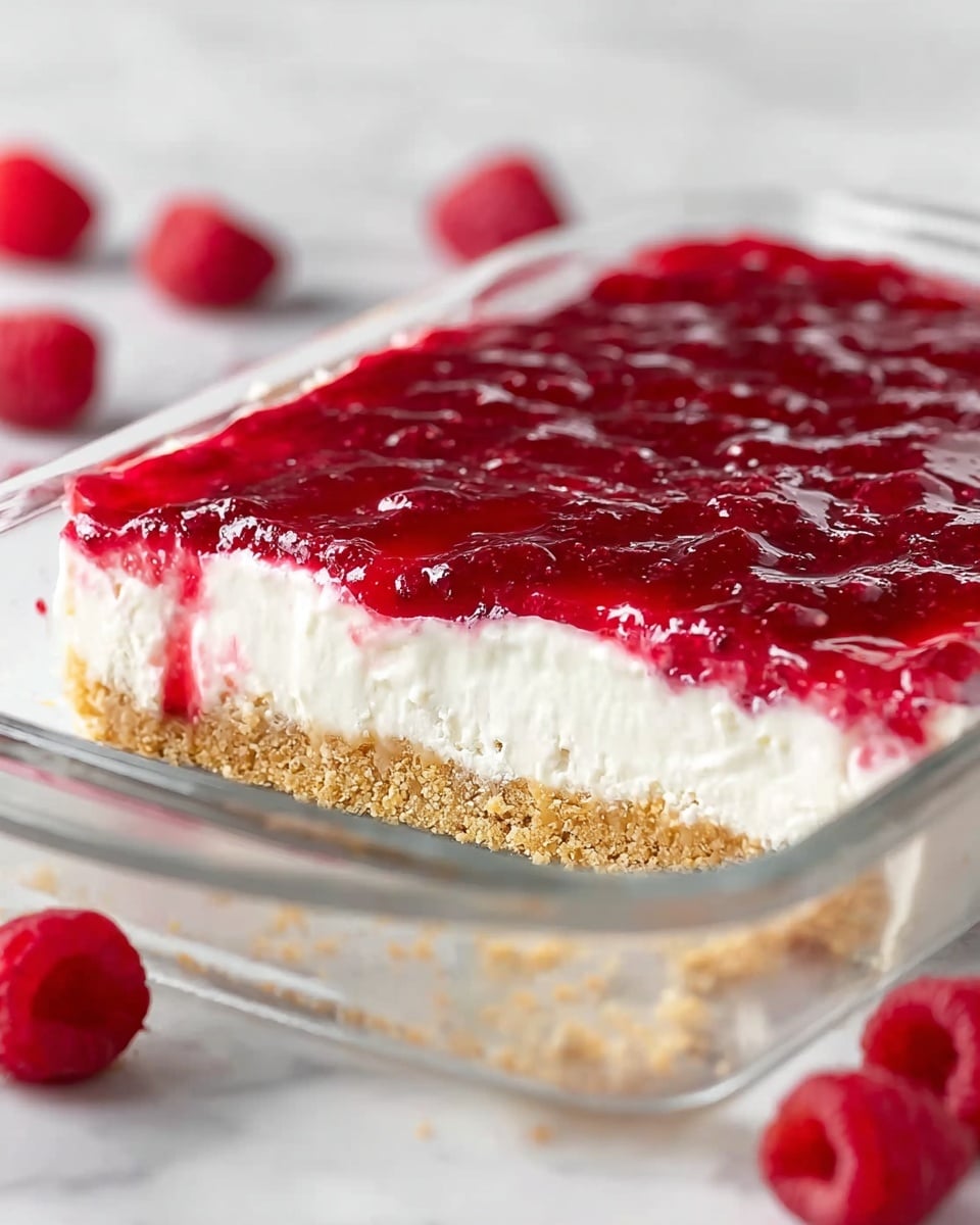 A rectangular glass dish holds a three-layer dessert placed on a white marbled surface. The bottom layer is a crumbly, light tan crust that looks slightly rough in texture. The middle layer is thick, creamy, and bright white, with a smooth and soft texture. The top layer is a shiny, bright red fruit jelly filled with visible small chunks of fruit, giving it a slightly bumpy surface. Around the dish, small red berries are scattered softly blurred in the background. Photo taken with an iphone --ar 4:5 --v 7