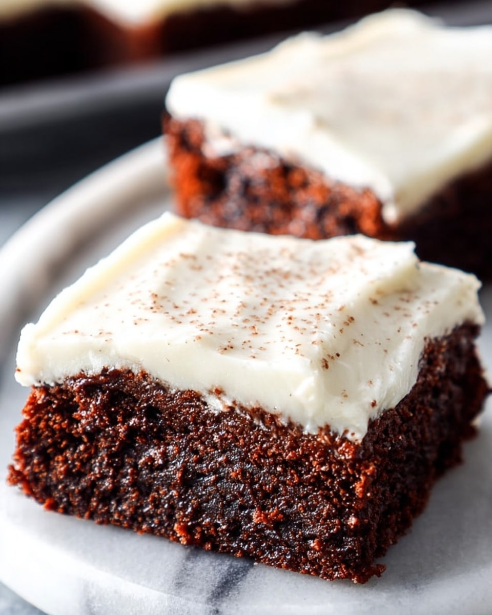 Two rich, moist chocolate brownies are shown on a white plate with a white marbled surface underneath. Each brownie has a thick, dark brown base layer that looks soft and dense, topped with a smooth, creamy white frosting layer. The frosting has some light brown specks sprinkled on top, adding texture. The brownies are cut into square shapes with clean edges. Photo taken with an iphone --ar 4:5 --v 7