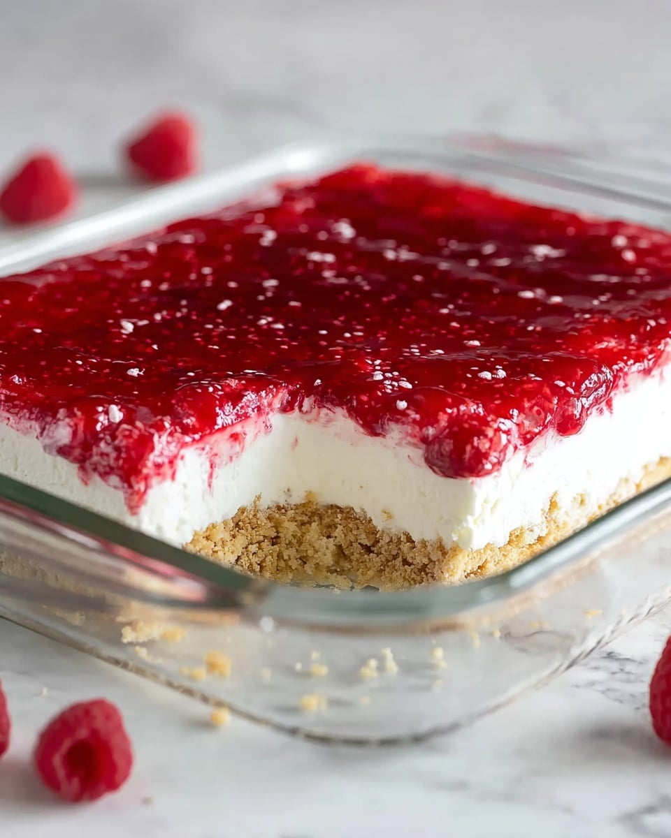 The image shows a clear rectangular glass baking dish filled with three distinct layers of dessert. The bottom layer is a crumbly, light golden brown crust that looks firm and slightly rough in texture. The middle layer is thick, creamy, and white, appearing soft and smooth, like whipped cream or a cream cheese mixture. The top layer is a bright red, glossy raspberry sauce with visible fruit pieces, slightly uneven on the surface and extending to the edges of the dish. The dish is placed on a white marbled surface with a few raspberries scattered around in the background. photo taken with an iphone --ar 4:5 --v 7