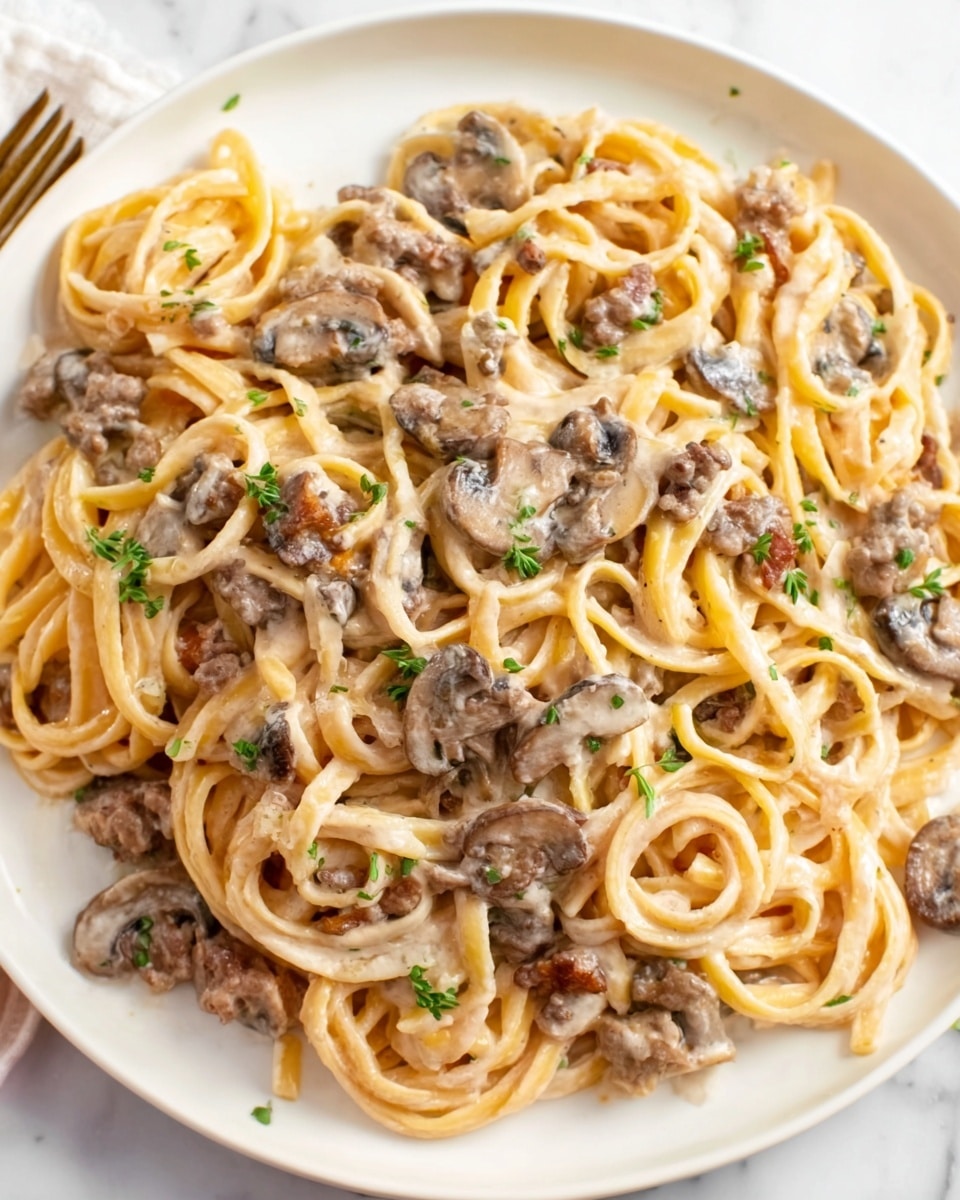 A white plate holds a serving of creamy pasta mixed with small pieces of browned ground meat and sliced mushrooms. The pasta is coated evenly with a thick, light beige sauce that looks smooth and rich. The meat bits and mushrooms are spread throughout the dish, adding darker brown and light tan colors that contrast with the pale pasta. Small green herbs are sprinkled lightly on top, giving a subtle touch of freshness. The plate sits on a white marbled surface, making the warm colors of the pasta stand out. Photo taken with an iphone --ar 4:5 --v 7