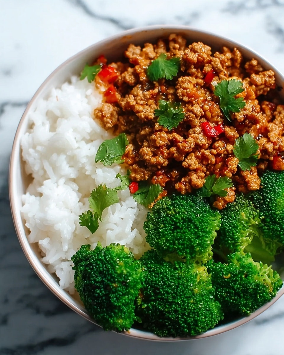 A white bowl contains three main layers, arranged side by side: bright green broccoli florets on the right with a rough texture, a mound of fluffy white rice on the left, and in the center a serving of glossy brown ground meat mixed with small bits of red pepper, garnished with scattered fresh green herb leaves. The bowl sits on a white marbled surface. Photo taken with an iphone --ar 4:5 --v 7