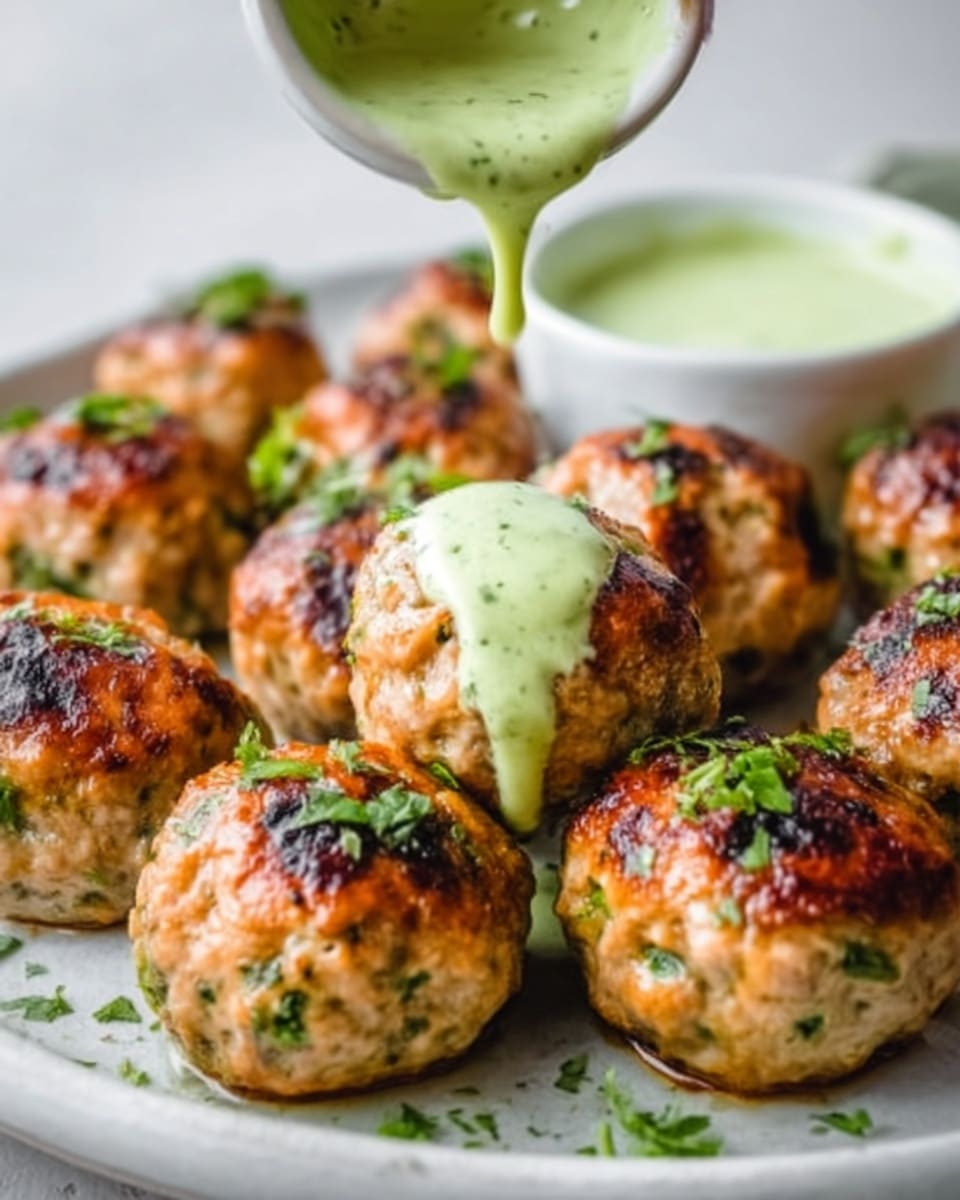 The image shows a close-up of eight round grilled meatballs arranged on a white plate with a white marbled background. Each meatball is golden brown with char marks and small green herb pieces visible inside. A creamy green sauce is being poured over the top center meatball by a woman's hand, and some of the sauce drips down the sides of several meatballs, adding a smooth texture. Fresh green herbs are sprinkled on top and around the plate, adding contrast to the warm colors of the meatballs. On the side, there is a small white bowl filled with more green sauce. The photo looks bright and fresh, captured with an iphone --ar 4:5 --v 7