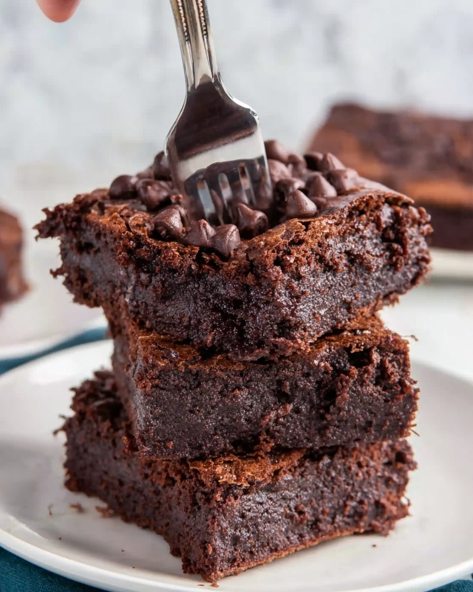 The image shows a stack of three thick, fudgy chocolate brownies on a white plate. Each brownie has a dark, rich brown color with a dense and moist texture. The top layer of each brownie is covered with a slightly cracked surface and generously sprinkled with shiny chocolate chips. A fork is stuck into the top brownie, with a woman's hand holding it from above. The background is a white marbled surface. photo taken with an iphone --ar 4:5 --v 7