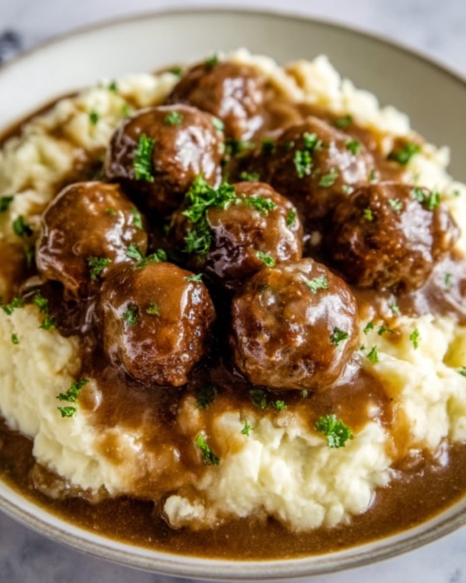 A white plate filled with creamy mashed potatoes covering the bottom layer, topped with several round, brown meatballs that are coated in a thick, dark brown gravy; small pieces of green parsley are sprinkled over the meatballs for color contrast. The mashed potatoes have a smooth, creamy texture, while the meatballs look tender and moist, sitting closely together on the plate. The sauce has a glossy finish, flowing a bit onto the edges of the potatoes. The background is a white marbled texture. Photo taken with an iphone --ar 4:5 --v 7