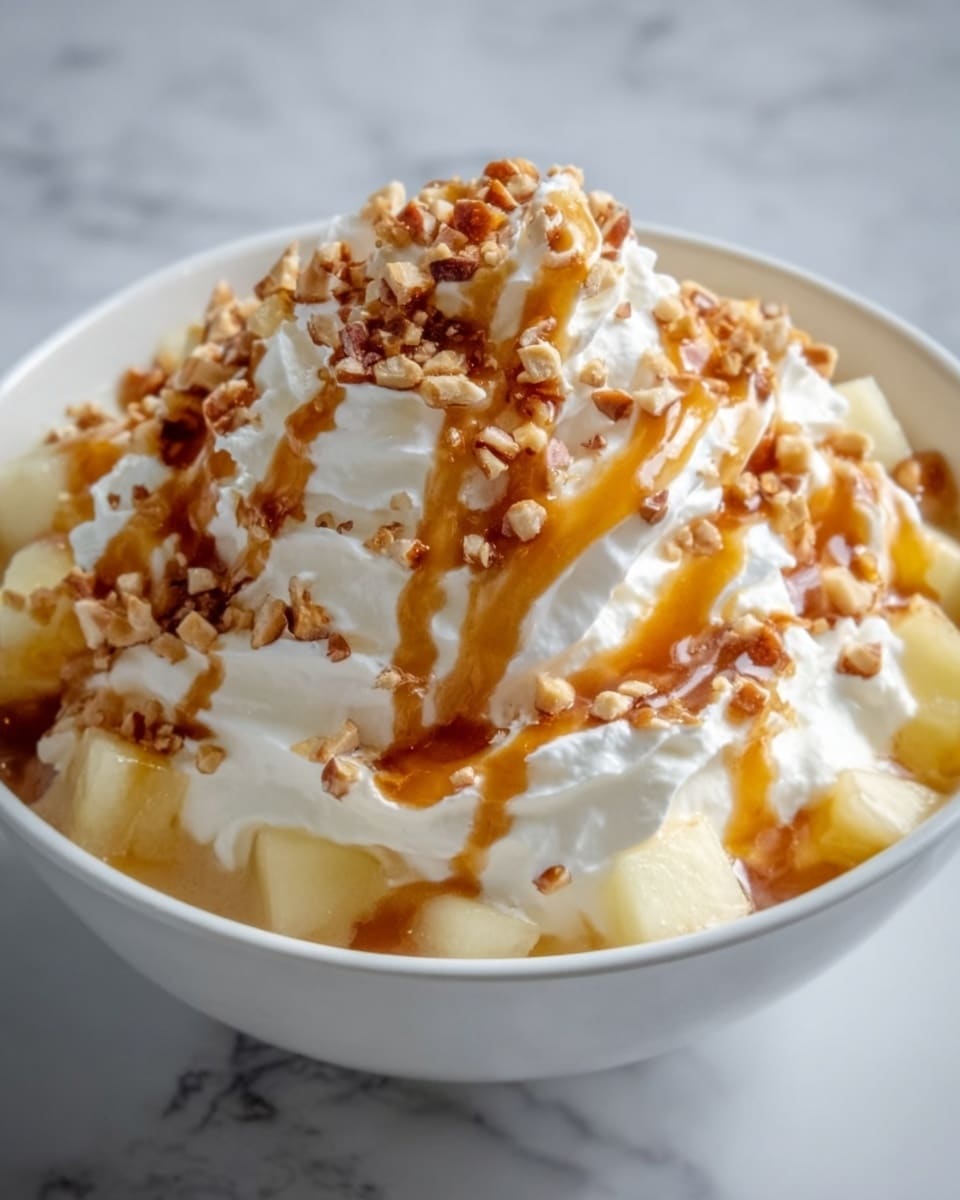 A white bowl filled with a creamy dessert that has multiple layers: the bottom layer is small, light yellow fruit cubes, followed by a thick layer of smooth white cream. On top, there are large dollops of whipped cream with a soft, fluffy texture. The dessert is drizzled generously with a rich, amber caramel sauce and sprinkled with small crunchy brown nut pieces that add texture. The bowl sits on a white marbled surface. photo taken with an iphone --ar 4:5 --v 7