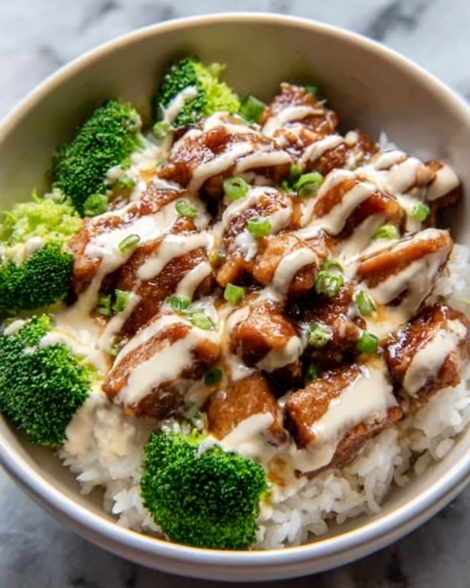 A white bowl filled with a bed of white rice at the bottom, topped with bright green steamed broccoli florets placed on one side. Above the rice and broccoli, there are several pieces of glazed chicken with a shiny, dark brown sauce, arranged in a neat row. The chicken is drizzled evenly with a creamy beige sauce, creating a striped pattern over the top. The food looks fresh and colorful against the white marbled textured surface. Photo taken with an iphone --ar 4:5 --v 7
