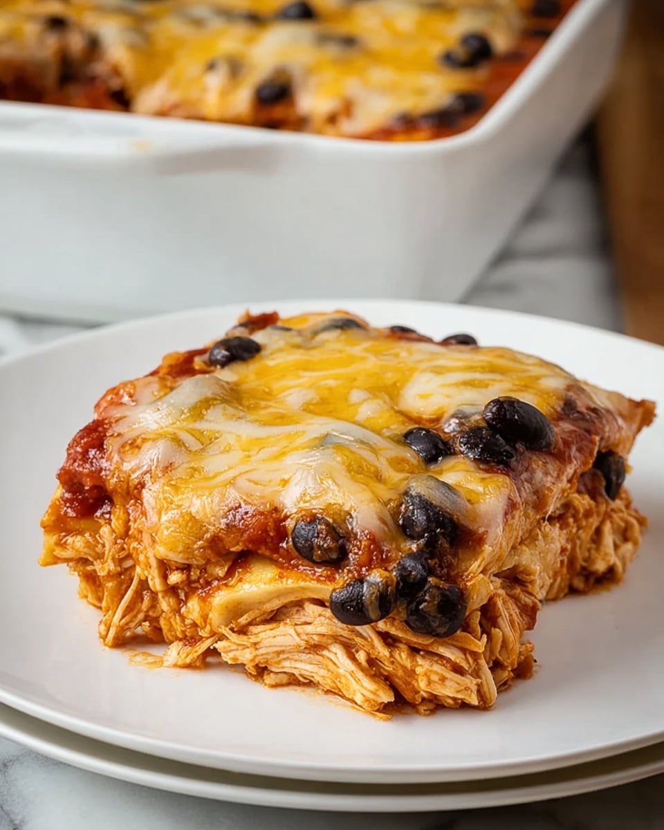 The dish shows a square piece of layered chicken enchilada on a white plate with a white marbled texture underneath. The bottom layer consists of shredded pale orange chicken mixed with sauce, followed by a middle layer with black beans scattered evenly throughout. On top of the beans lies a rich red sauce layer blanketed by a thick layer of melted yellow and light brown cheese that stretches slightly on one side. The whole piece looks moist with cheese bubbling lightly, while in the background part of a white rectangular baking dish filled with more of the same enchilada is visible. Photo taken with an iphone --ar 4:5 --v 7