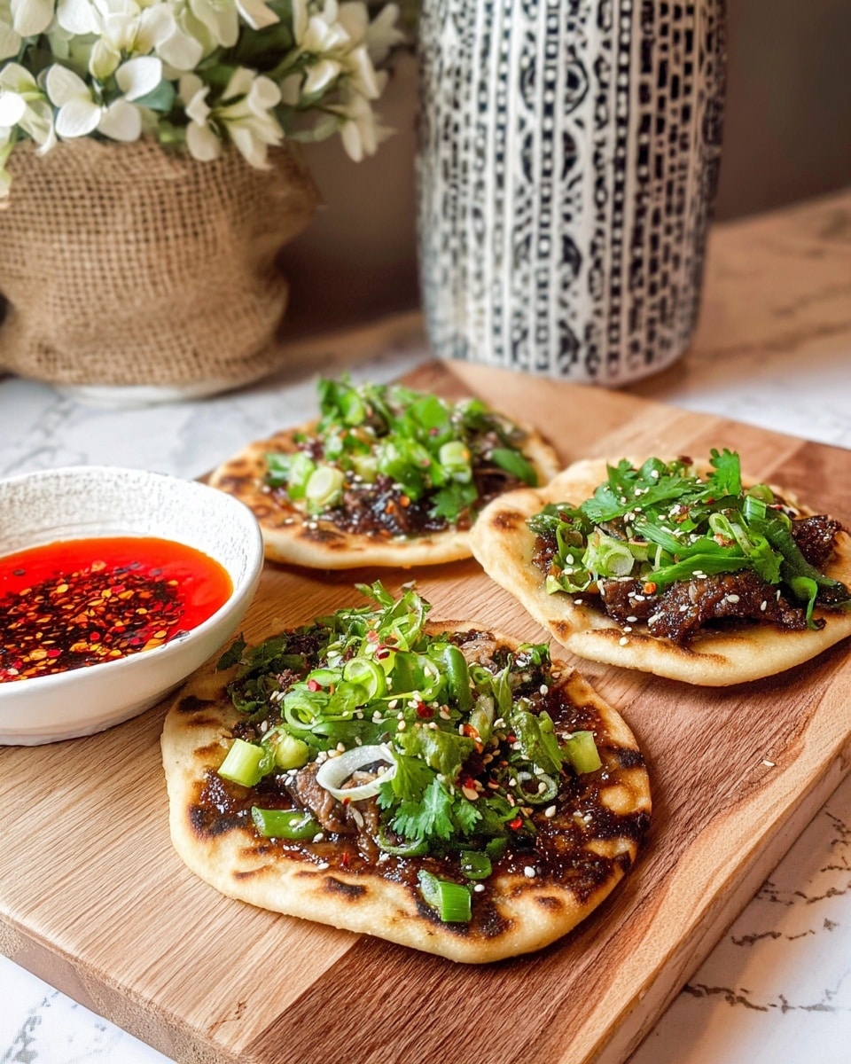 The image shows three small flatbreads on a wooden board, each topped with a dark, slightly charred layer of meat or sauce, giving a textured and rich brown look. On top of this base layer, there are fresh green garnishes including thinly sliced green onions curled into rings and chopped cilantro, sprinkled with sesame seeds. To the left, there is a small white bowl with bright red chili oil sauce, filled with visible chili flakes. In the background, there is a burlap bag with white flowers and a white vase with black patterns, all set on a white marbled surface. photo taken with an iphone --ar 4:5 --v 7