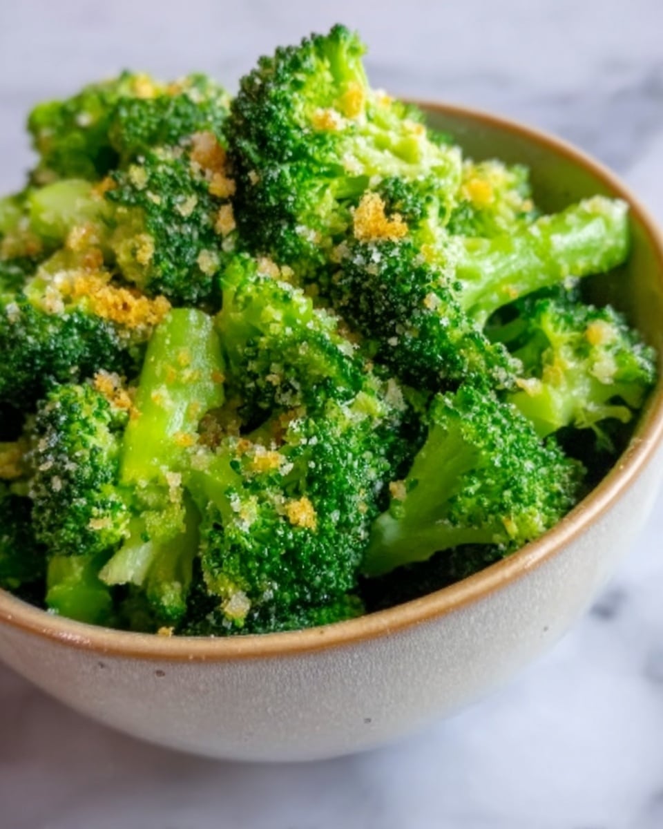 A close-up image shows a white bowl filled with bright green broccoli florets mixed with small bits of a yellow topping, possibly cheese or breadcrumbs. The broccoli looks fresh and cooked, with a slightly rough texture from the topping. The bowl sits on a white marbled surface, creating a clean and simple background. Photo taken with an iphone --ar 4:5 --v 7