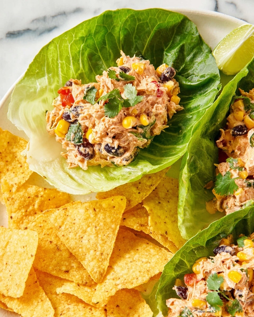 The image shows two lettuce wraps with three layers each: first, a large green lettuce leaf with detailed veins and a fresh look; second, a creamy mix of shredded chicken, black beans, yellow corn, small red pepper pieces, and fresh herbs giving a mix of cream, yellow, black, red, and green colors; third, a few small cilantro or parsley leaves on top for a fresh green touch. The wraps are placed on a white plate, surrounded by light yellow, triangular corn chips with a rough texture, and there is a lime wedge on the side. The background is a white marbled texture. photo taken with an iphone --ar 4:5 --v 7