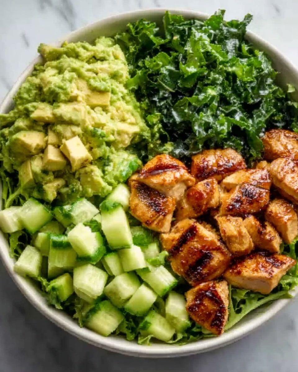A white bowl filled with four distinct sections: one side has grilled chicken pieces with golden brown, slightly charred grill marks and a glossy texture; next to it is a bright green chunked avocado layer with visible creamy texture; another part holds dark green chopped kale leaves with a slightly rough texture; and the last section has fresh cucumber cubes showing a lighter green with a smooth, shiny surface. The bowl sits on a white marbled surface. Photo taken with an iphone --ar 4:5 --v 7